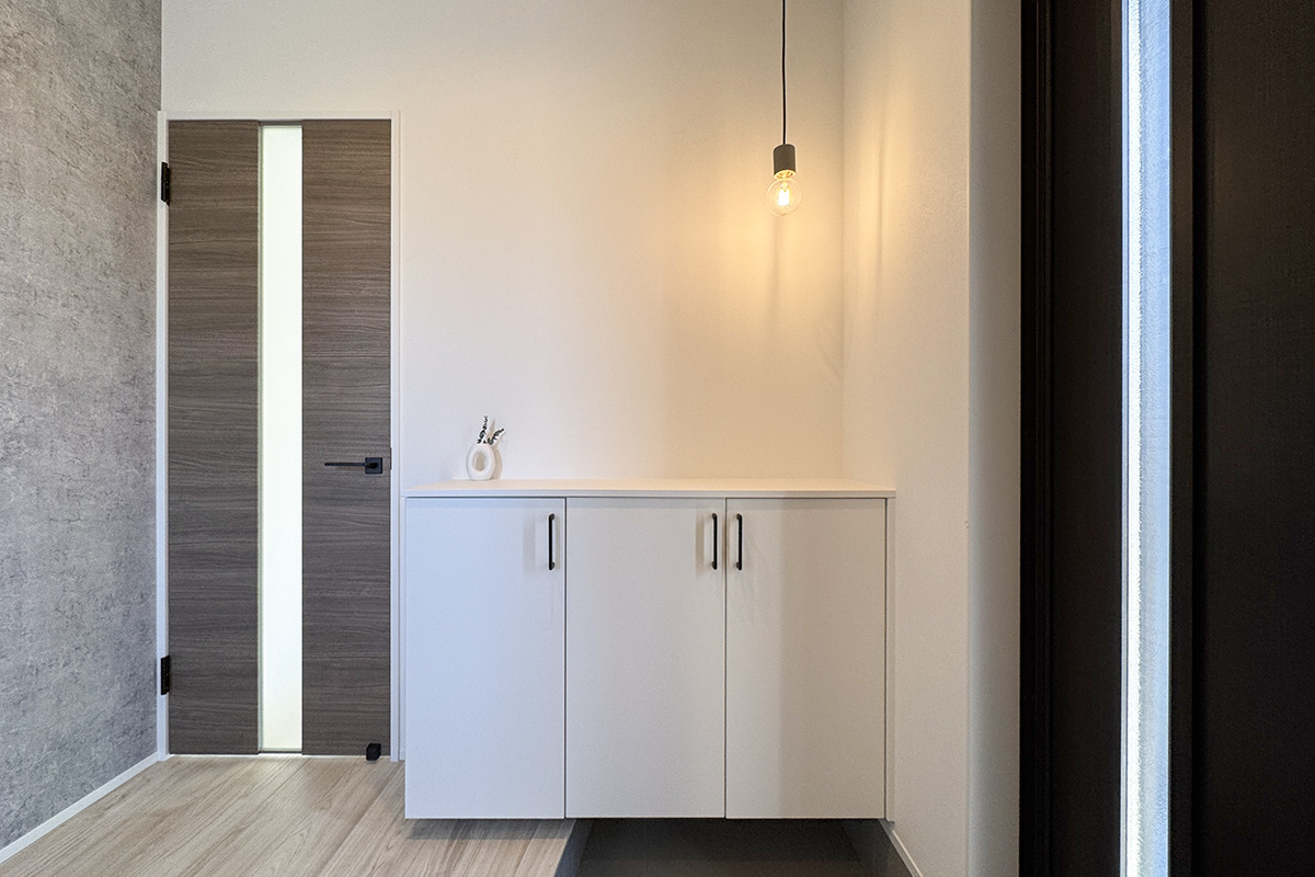 モルタル調のアクセントクロスが印象的な玄関。ペンダントライトでオシャレな空間に。